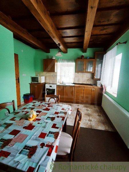 A kitchen in a family house with a wooden beam ceiling, a table, and green walls.