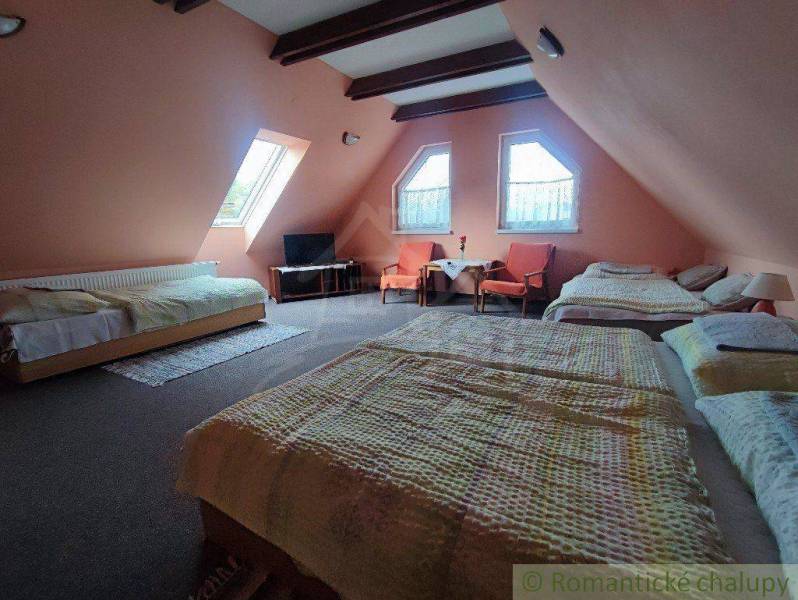 The attic bedroom offers three beds, a television, and a seating area, suitable for a family house.