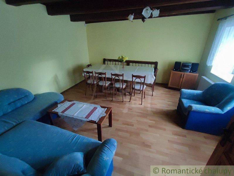 Living room with wooden ceilings, a blue sofa, a dining table, and yellow walls in a family house.