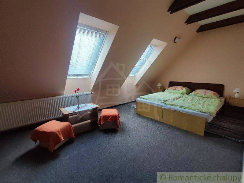 Attic bedroom with a double bed, skylights, orange chairs, and a table.