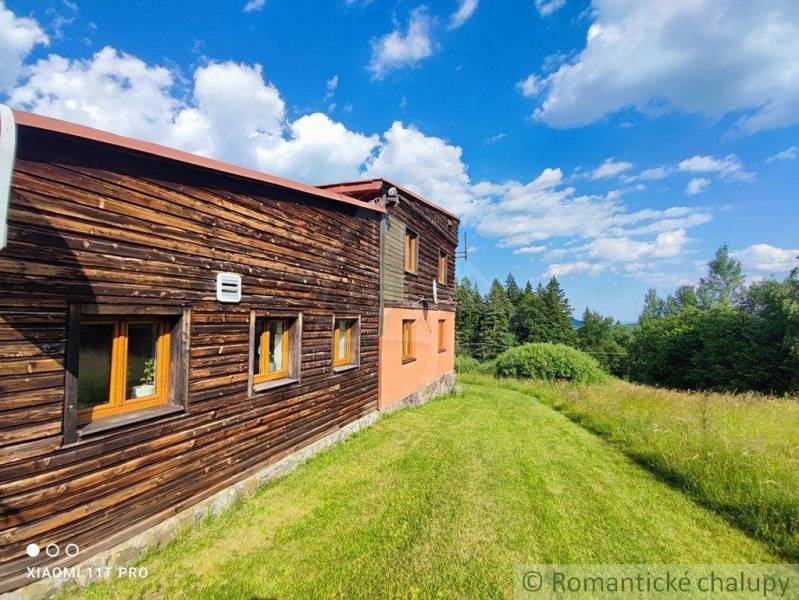 A family house with a wooden facade surrounded by a green meadow and a blue sky.