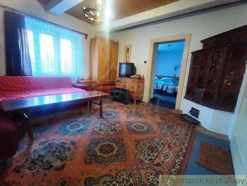 Living room with a tiled stove, wooden furniture, carpet, and television in a family house.