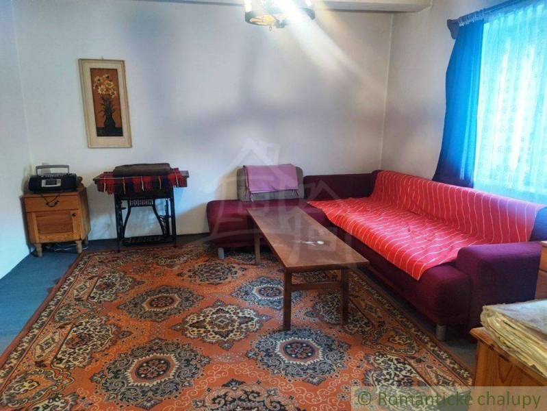 Living room with an old carpet, sofa, table in a family house, decorated with a painting and a curtain.