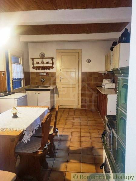 We see a traditional kitchen in an old family house with a tiled stove and wooden furniture.