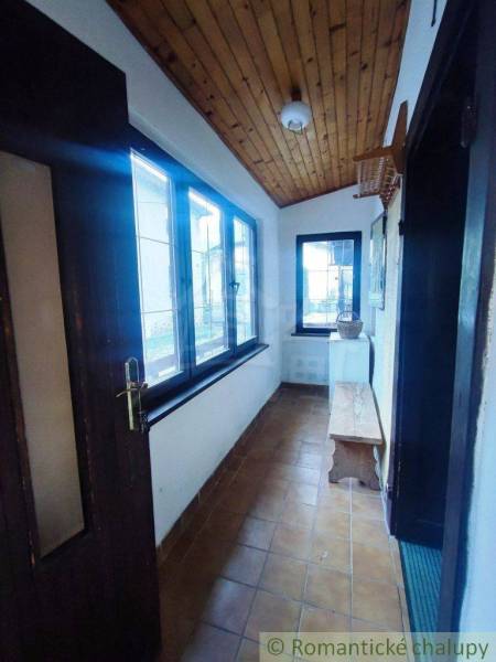 A narrow interior with a wooden ceiling, tiles, and a bench in a family house.