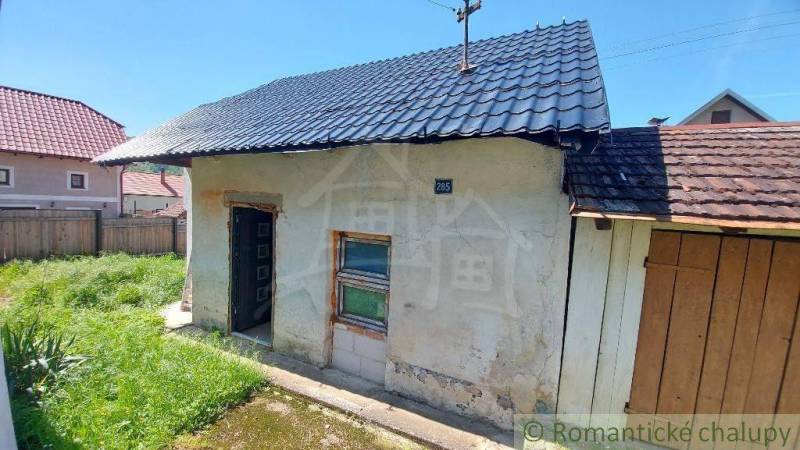 An older family house with a garden and a metal roof, surrounded by a wooden fence.
