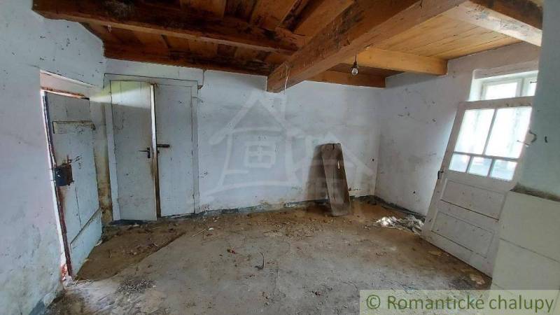 An old interior of a country cottage with ceiling beams and worn walls.
