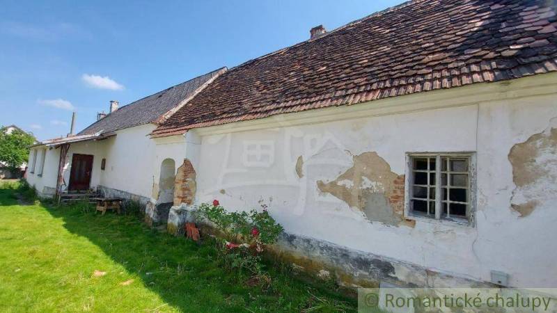 An old village family house with peeling plaster, sloping roof, green lawn.