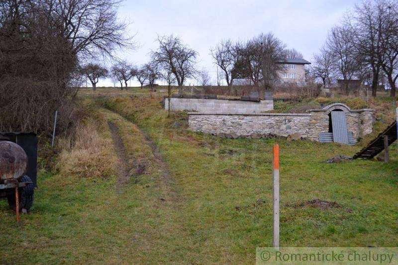 A dirt road leads to the house, surrounded by trees and a stone cellar in the garden.