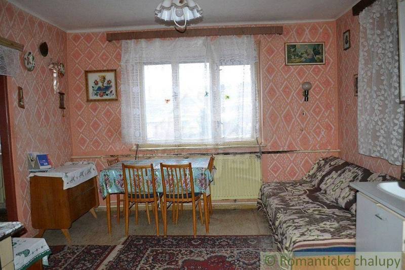 A room in an older family house with a sofa, table, chairs, and patterned wallpaper.