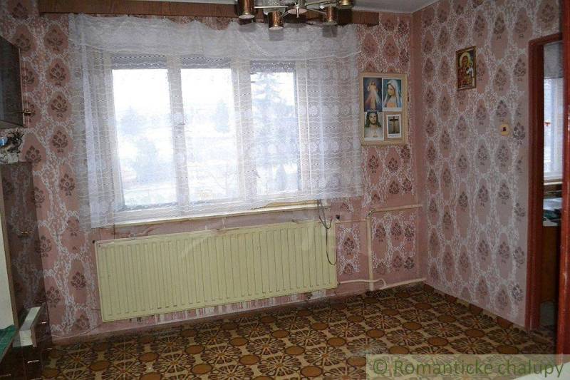 A family house with floral wallpaper, a large window, and religious paintings on the wall.