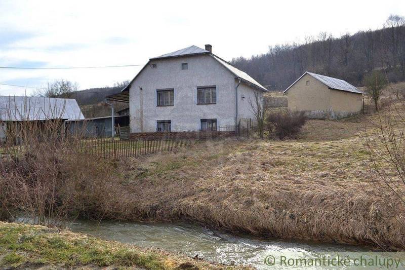 A family house by a stream in the countryside, surrounded by grassy areas in nature.