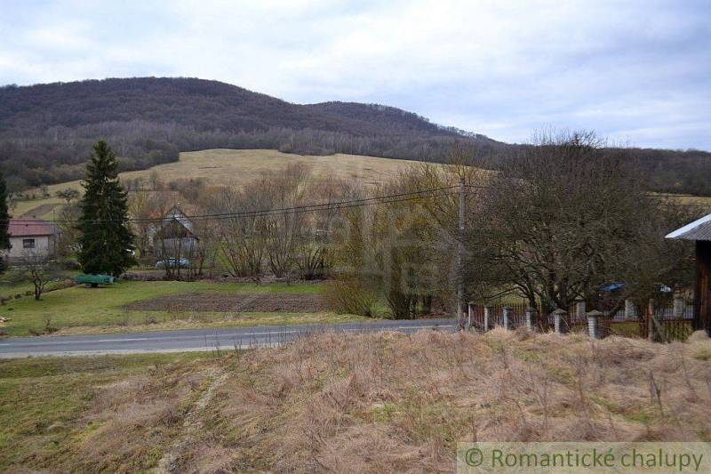A rural view of agricultural and forest lands, surrounded by mountains and a road.