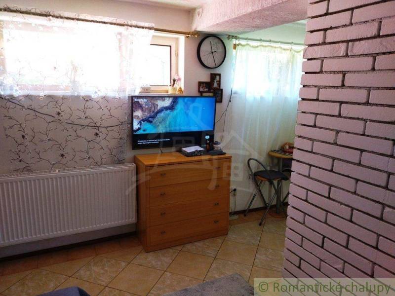 Television in the corner of the room next to the clock, masonry, furniture, blinds, and a family house.