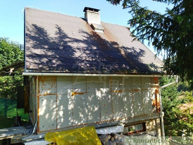 A family house with a sloped roof, surrounded by trees, with renovation work taking place nearby.
