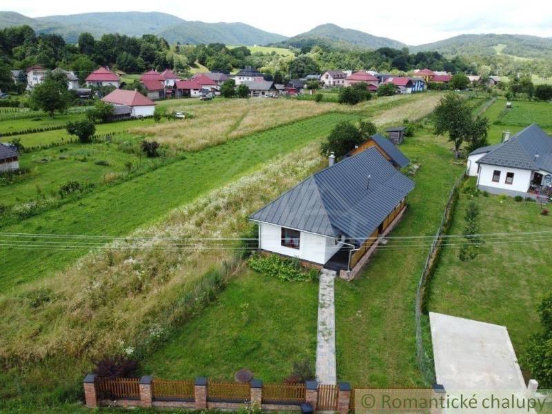 A wooden cottage surrounded by picturesque countryside and mountains on the horizon.