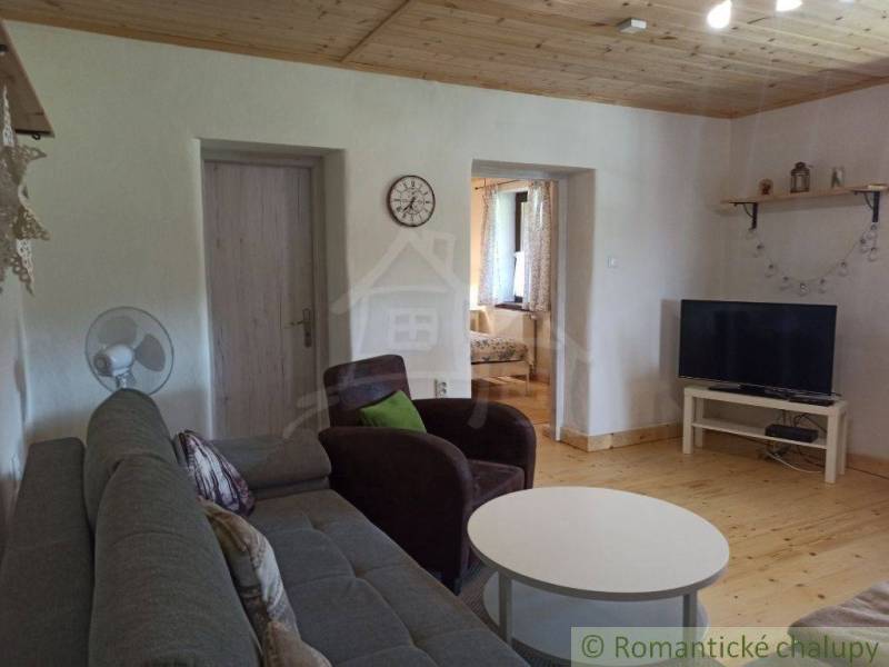 A living room in a cottage with a sofa, television, and wooden ceiling, ideal for relaxation.