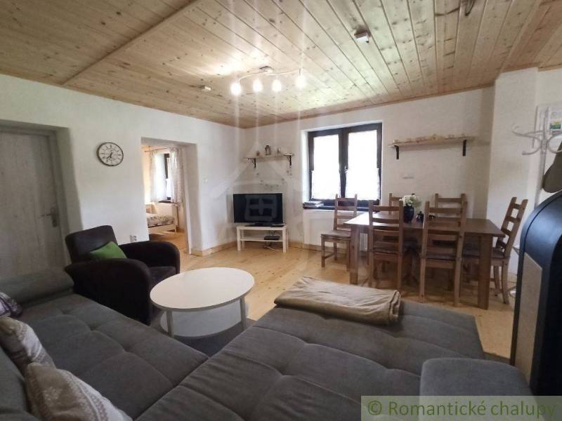Living room in a cozy cabin with a wooden ceiling, sofa, and dining table.