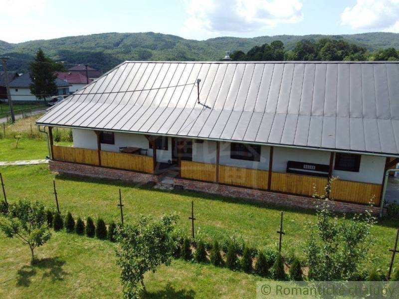 A cottage in picturesque nature with wooden verandas and a roof, surrounded by a garden with coniferous trees.