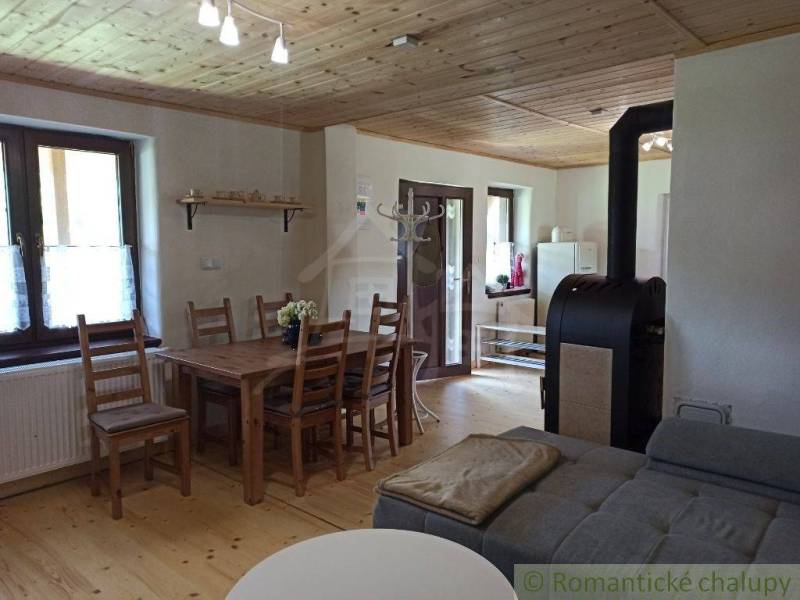 A rustic cottage with a wooden ceiling, a dining table, and a fireplace in a cozy setting.