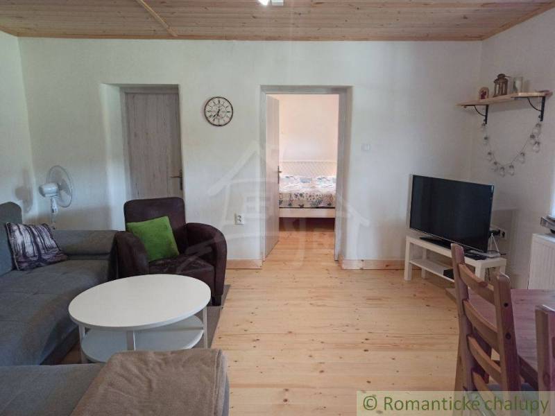 Living room of the cottage with wooden flooring, a sofa, a television, and a dining table.