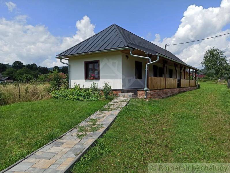 In the picture, there is a country cottage with a porch and a paved path in a natural setting.