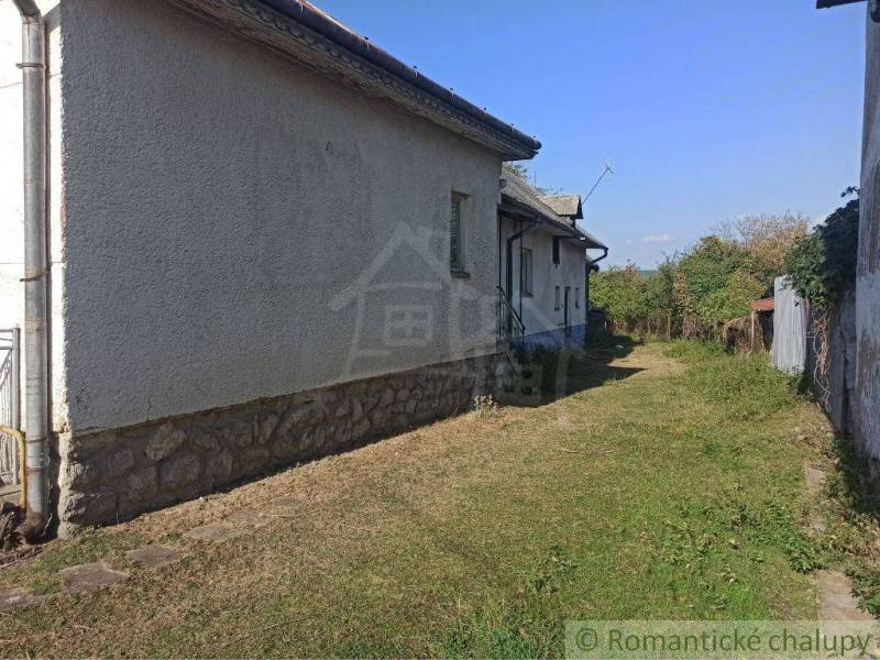 A family house with white plaster, a stone foundation, surrounding garden, and blue sky.