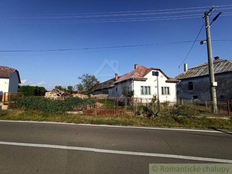 A country house, an older house with a metal roof, a fenced plot by the road.