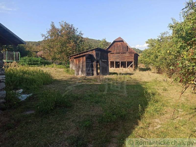 Garden area with a wooden cottage and a family house in a picturesque natural setting.