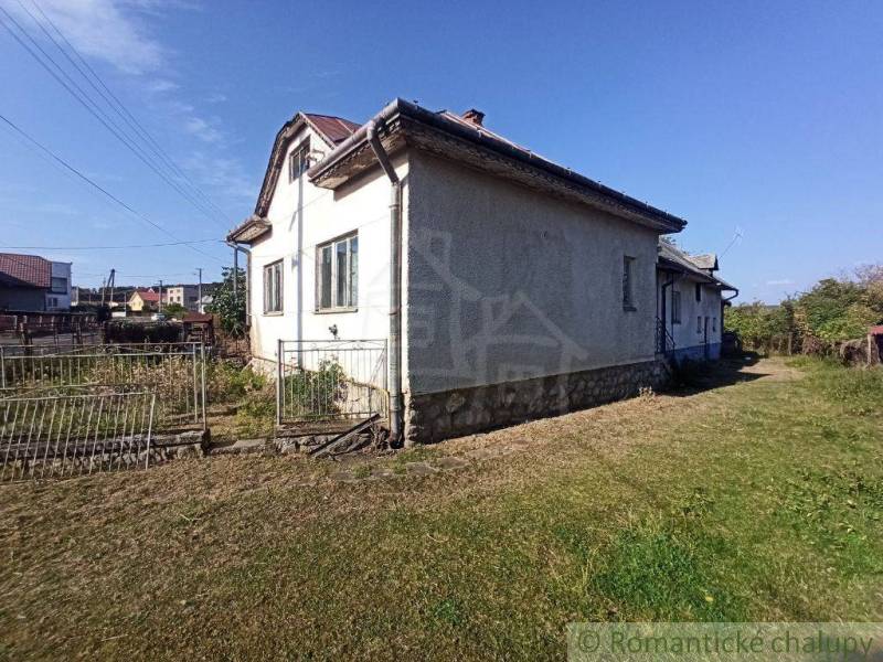 In the picture, there is an older family house with a lawn and a fence, surrounded by a garden.