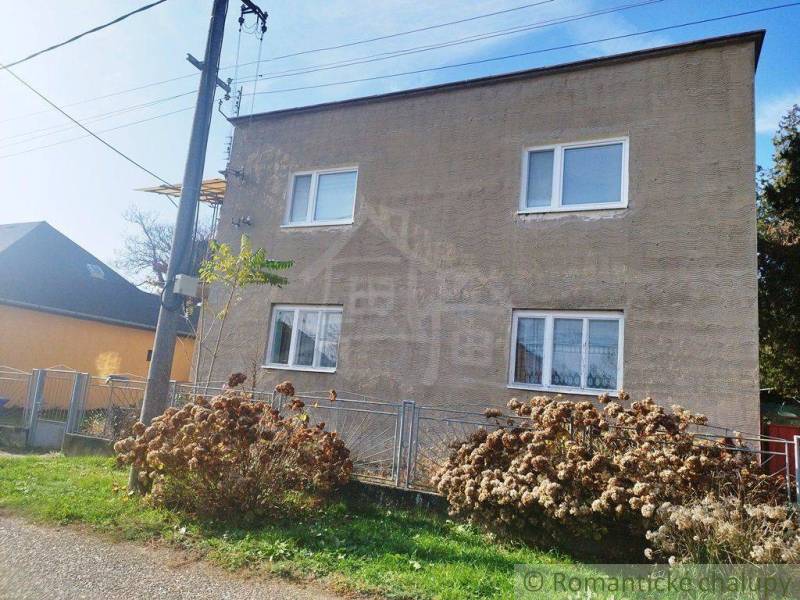 A family house with a gray facade, windows, an electric pole, and a fence.