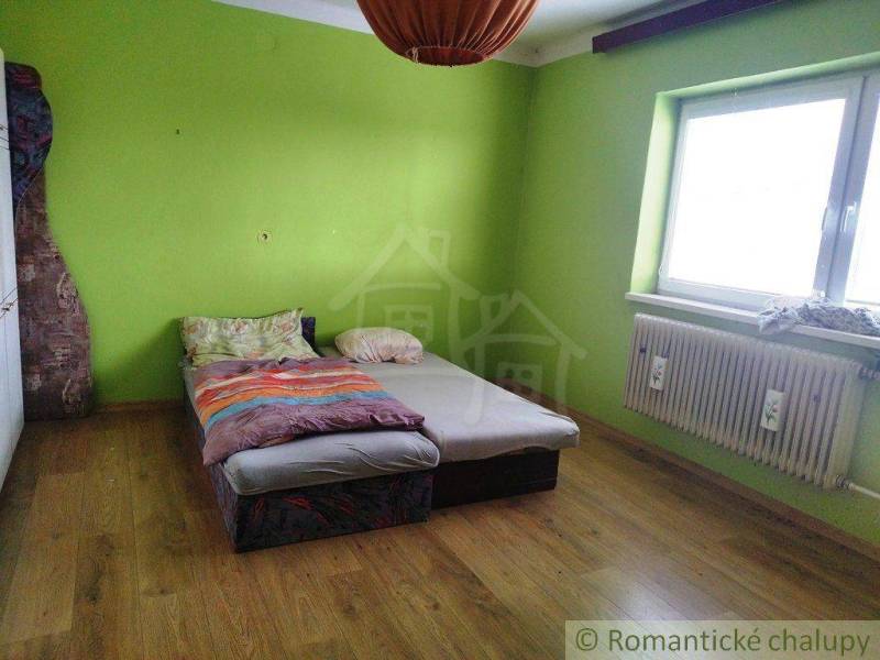The green room in the family house has a wooden floor and a simple bed.
