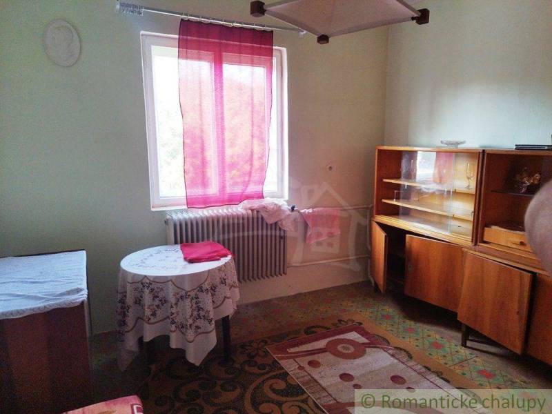 A room with vintage furniture, pink curtains, a table, and shelves in a family house.