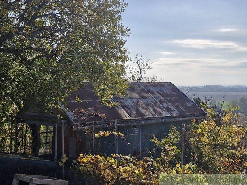 An old cottage in a natural setting with deciduous trees and a view of the surrounding landscape.