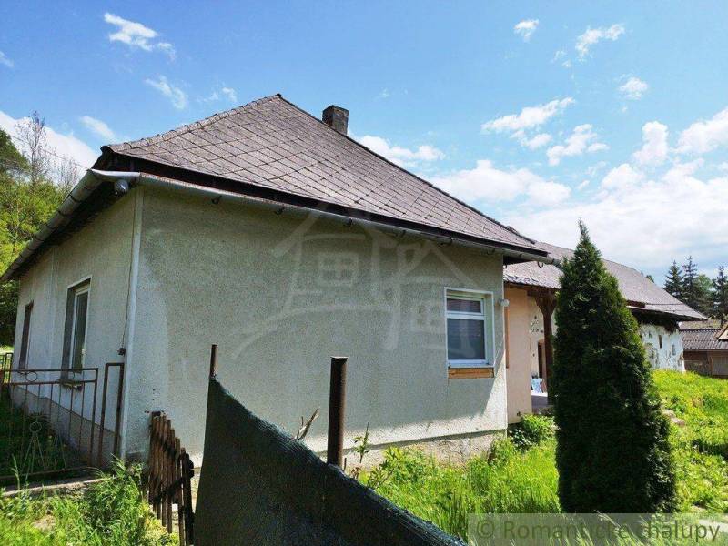 A cottage surrounded by nature with a classic roof and simple fencing.