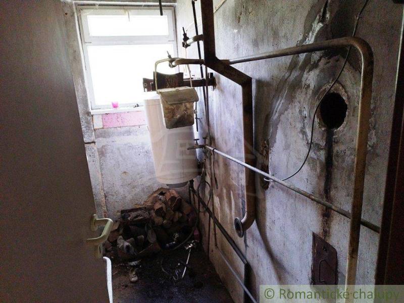 An old fireplace in the cottage with wood, a stove, and a dirty wall by the window.
