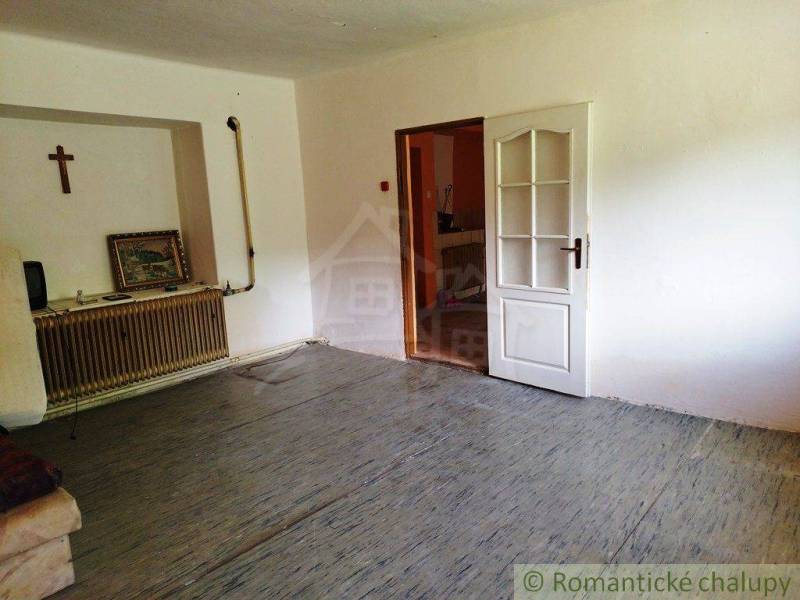 In the picture, there is a simple room with a cross, a radiator, and a painting in a cottage.