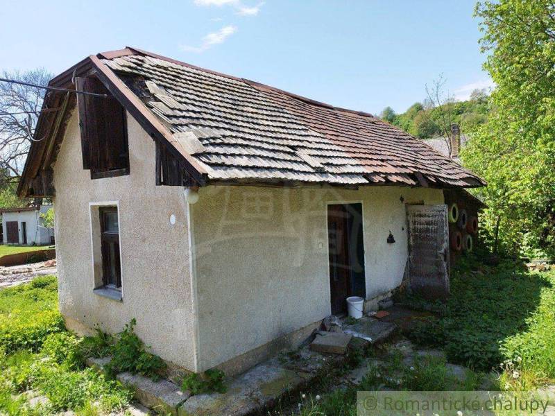 An old cottage with a damaged roof, surrounded by greenery, in a rural setting.