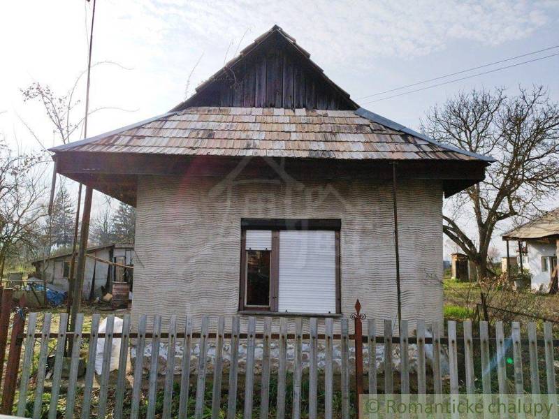 A traditional country cottage with a shingle roof and a fence in the garden.