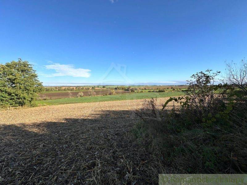 A wide panorama shows agricultural and forest lands, fields, bushes, and a blue sky.