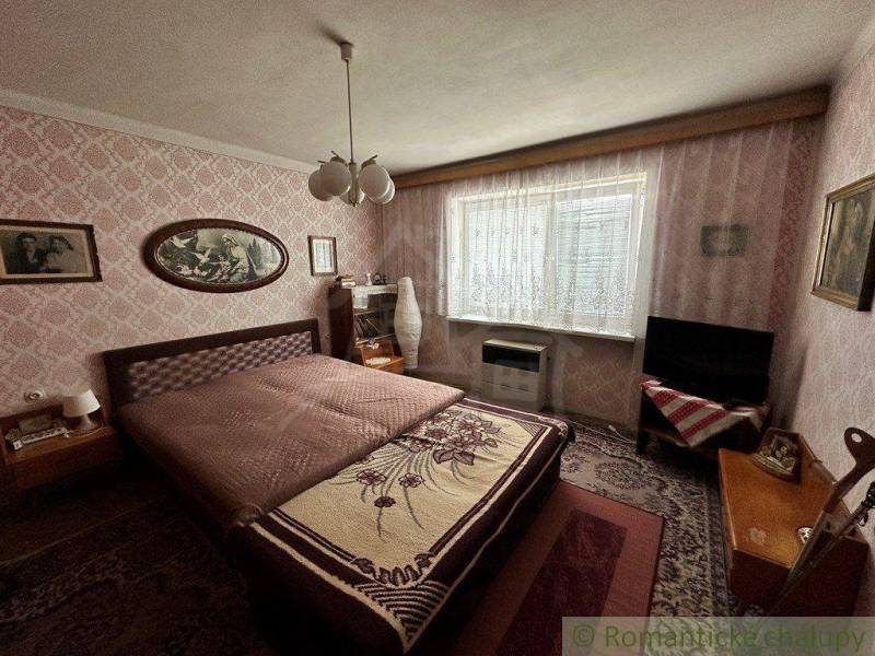 A bedroom in a family house with a floral blanket, vintage wallpaper, and classic furniture.