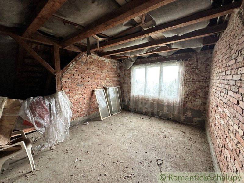 The attic of a family house with an exposed brick wall, old furniture, and a window frame.