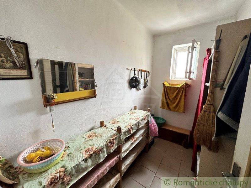 A narrow hallway with a window, a mirror, kitchen utensils, handmade decorations, furniture in a family house.