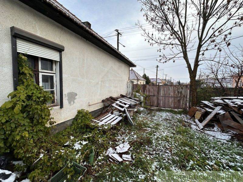 A family house with an unkempt yard, wood, and a gate covered in snow in winter.