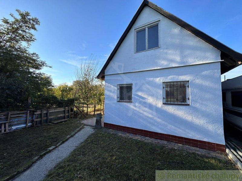 A white cottage with shutters in a yard surrounded by greenery, a typical Slovak scenery.