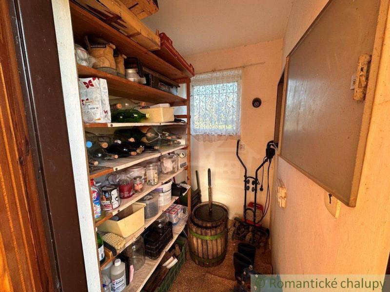 A small cellar with shelves filled with supplies, drinks, and tools near the cottage.
