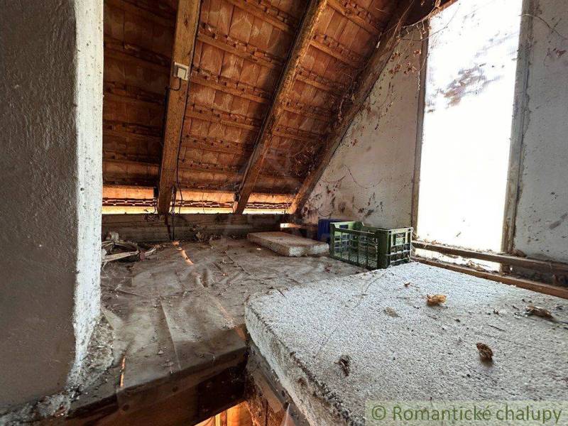 The attic of the cottage with a wooden roof truss and a view from the window of the surrounding landscape.