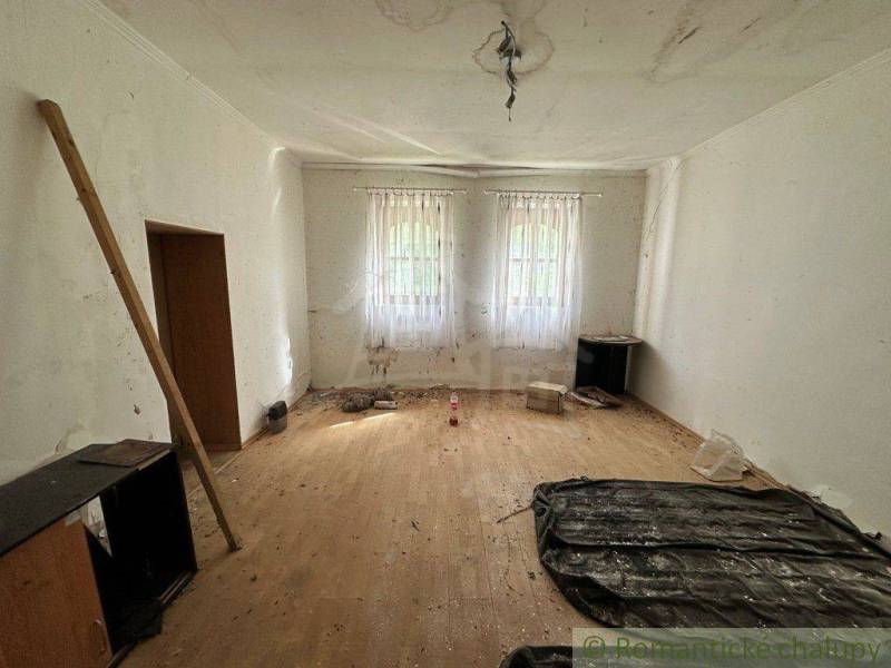 A room with wooden flooring, white walls, and windows with white curtains.