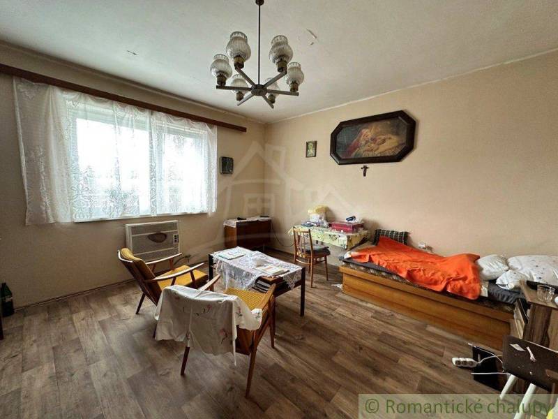 A room in a family house with armchairs, a bed, wooden flooring, and wall decorations.