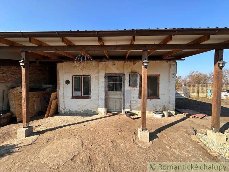 An old cottage with a porch and a wooden roof under a blue sky.